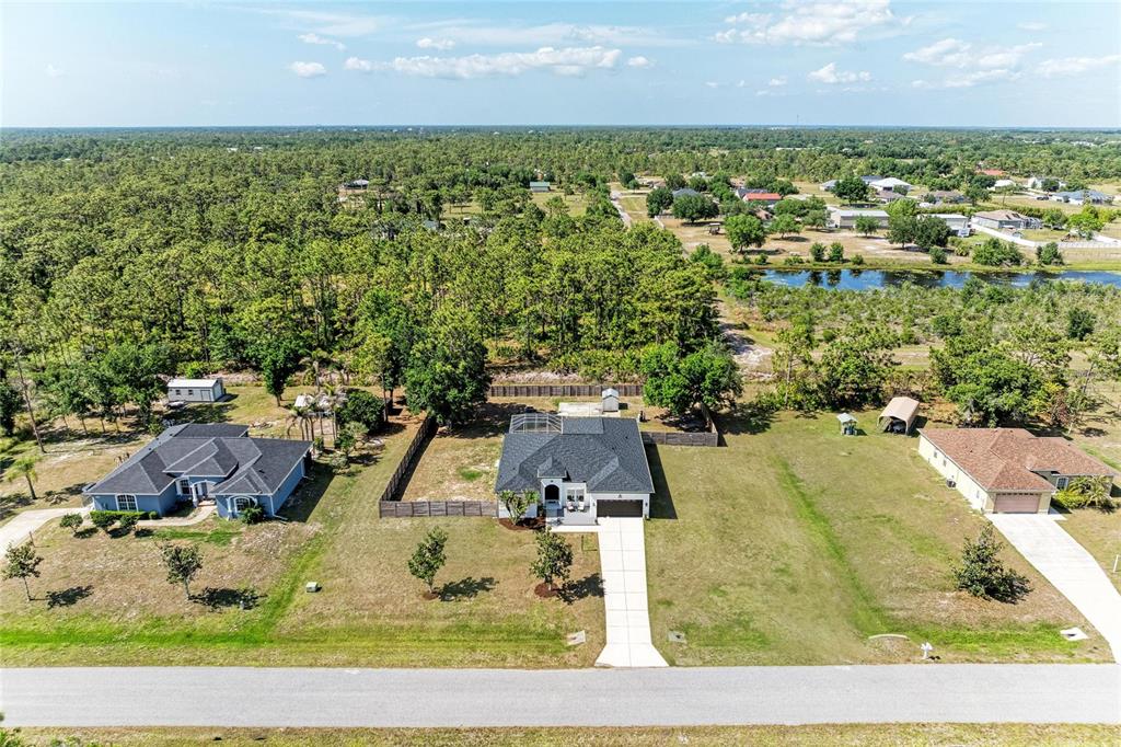 An aerial view shows three suburban houses surrounded by trees and a nearby pond — 26013 81ST DRIVE E, MYAKKA CITY, FL