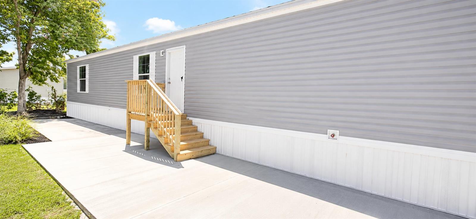The exterior of a manufactured home features gray horizontal siding, a white door, and wooden stairs — 820 Maryland Avenue, Clewiston FL 33440, CLEWISTON, FL