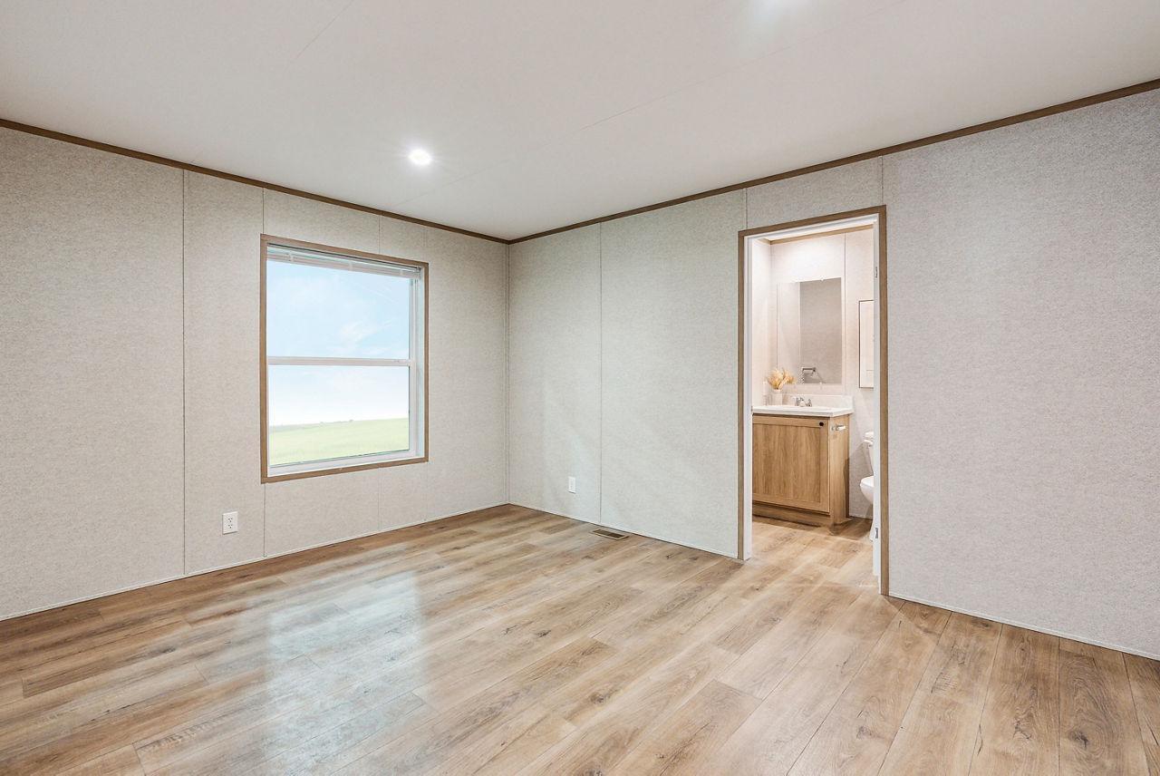 An empty bedroom with light wood-look flooring, neutral paneled walls, and an attached bathroom — 820 Maryland Avenue, Clewiston FL 33440, CLEWISTON, FL