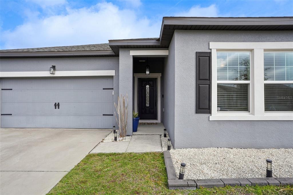 The exterior of a gray single-story house features a garage, front door, and gravel landscaping — 3522 FERNANDA DRIVE, DELTONA, FL