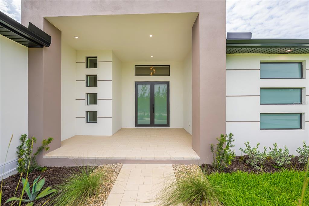 The exterior of a modern home features a covered entryway with double doors and windows — 16692 LIGGETT CIRCLE, PORT CHARLOTTE, FL