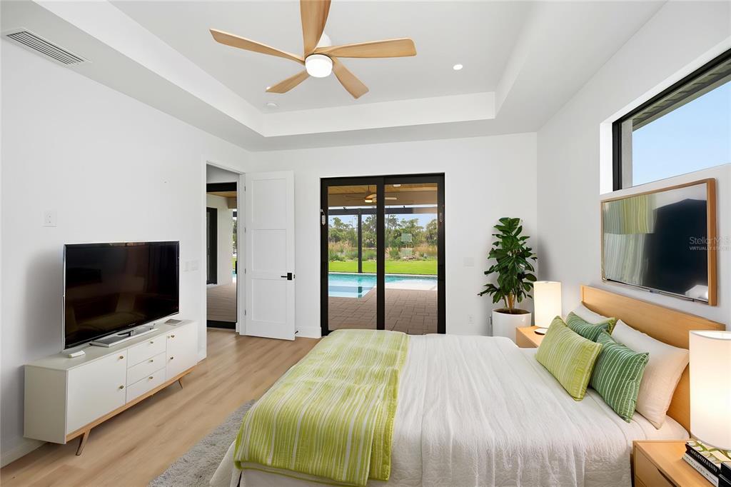 A modern bedroom features a tray ceiling, light wood floors, and sliding doors to a pool — 16692 LIGGETT CIRCLE, PORT CHARLOTTE, FL