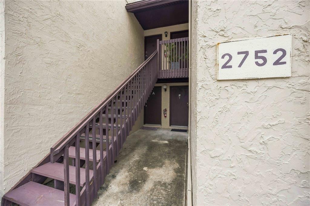 An exterior view of a two-story apartment building entrance with a wooden staircase — 2752 HIDDEN LAKE BOULEVARD UNIT C, SARASOTA, FL