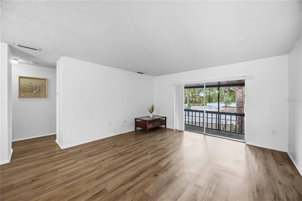 An empty living room features wood-look flooring, white walls, and a sliding glass door to a balcony — 2752 HIDDEN LAKE BOULEVARD UNIT C, SARASOTA, FL
