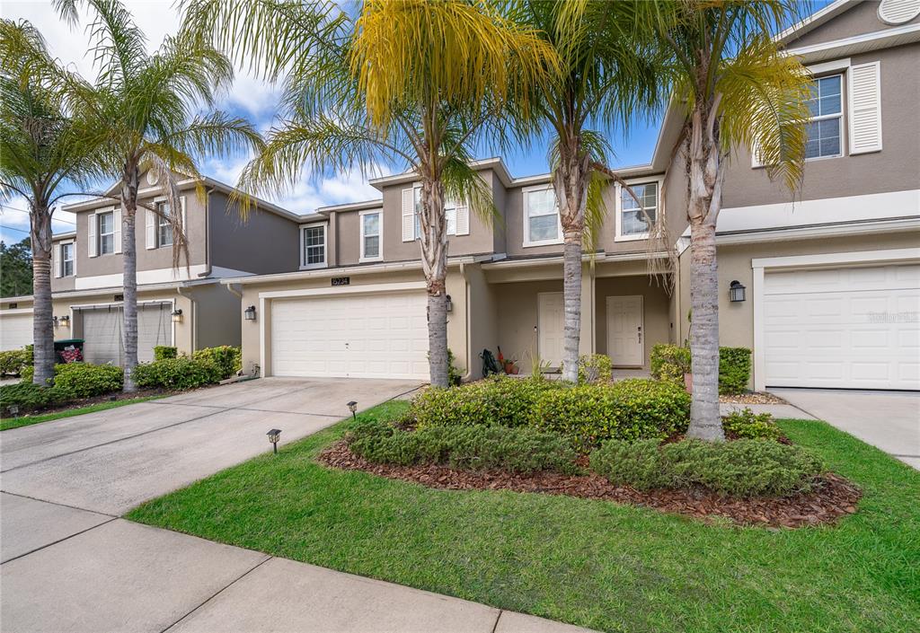 A row of two-story townhomes with beige stucco exteriors, attached garages, and palm trees in front — 15234 HARRINGTON COVE DRIVE, ORLANDO, FL