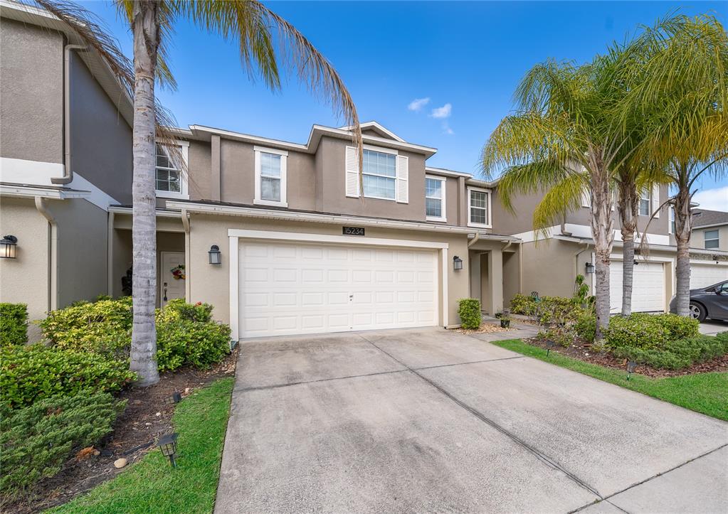 A two-story townhouse with a beige stucco exterior, a two-car garage, and palm trees — 15234 HARRINGTON COVE DRIVE, ORLANDO, FL