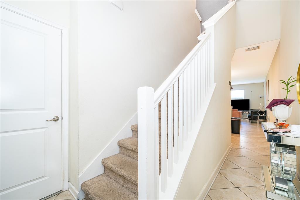 A carpeted staircase with a white railing stands next to a door in a hallway — 15234 HARRINGTON COVE DRIVE, ORLANDO, FL