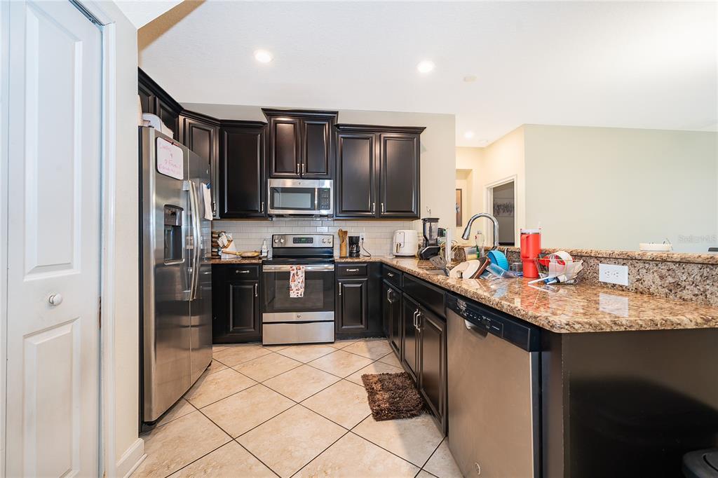 A kitchen features dark wood cabinets, granite countertops, stainless steel appliances, and tile flooring — 15234 HARRINGTON COVE DRIVE, ORLANDO, FL