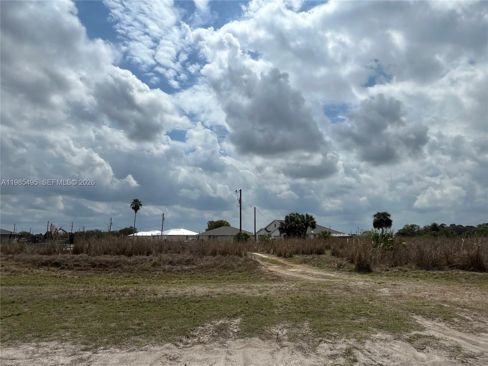 A dirt path leads through a grassy, undeveloped lot toward distant houses under a cloudy sky — 7025 Beaver Cir, La Belle FL 33935, LA BELLE, FL