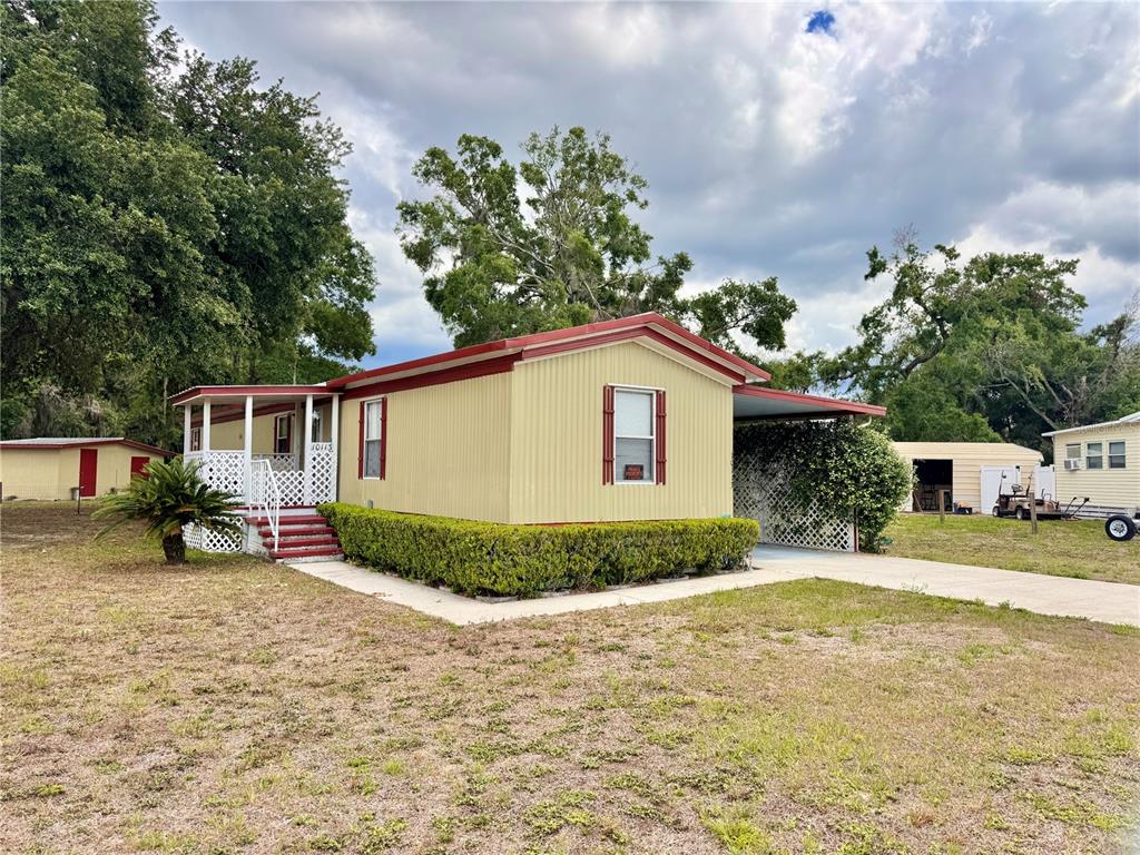 A yellow mobile home with a red roof, a front porch, and a side carport — 10113 SE 24TH DRIVE, WEBSTER, FL