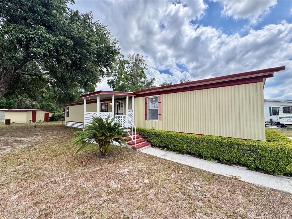 A single-story mobile home with tan siding, a red roof trim, and a small front porch — 10113 SE 24TH DRIVE, WEBSTER, FL
