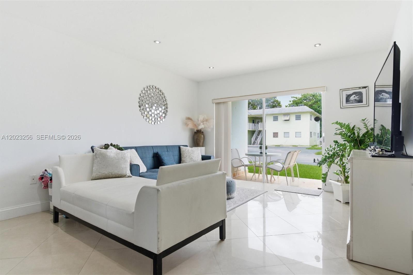 A living room with white tile floors, a white daybed, a blue sofa, and a patio — 7680 SW 82nd St # H121, Miami FL 33143, MIAMI, FL