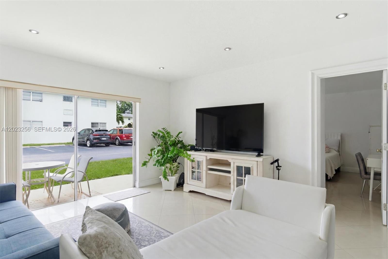 A living room with white tile floors, a television console, and a sliding glass door — 7680 SW 82nd St # H121, Miami FL 33143, MIAMI, FL