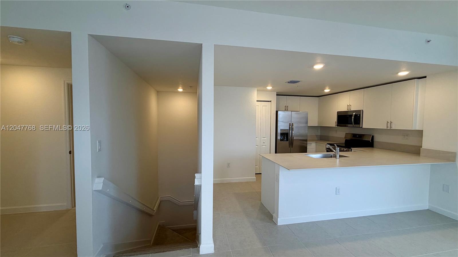 A kitchen with white cabinets and stainless steel appliances sits beside a carpeted staircase — 15601 SW 280 # 1, Miami FL 33032, MIAMI, FL
