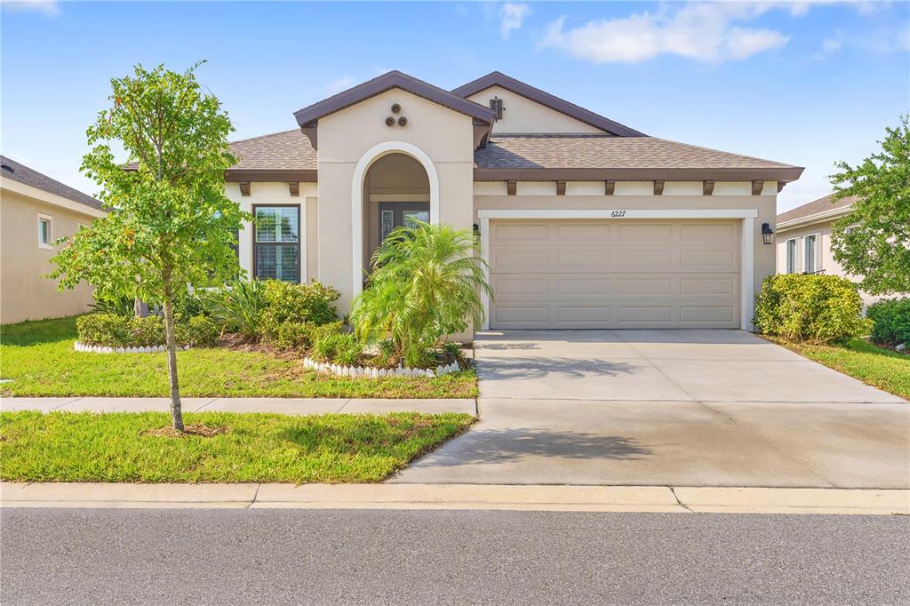 A single-story suburban house with a beige stucco exterior, a two-car garage, and landscaping — 6227 GOLDEN NETTLE DRIVE, APOLLO BEACH, FL