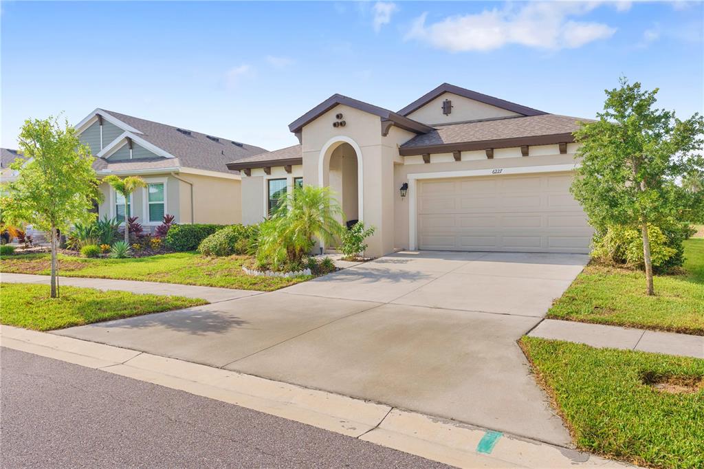 A single-story suburban house with a beige stucco exterior, a two-car garage, and a driveway — 6227 GOLDEN NETTLE DRIVE, APOLLO BEACH, FL