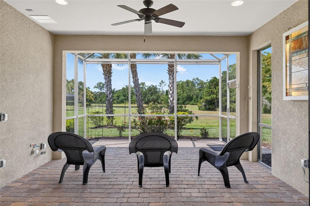 A screened-in patio with brick flooring, a ceiling fan, and three black chairs facing outdoors — 16748 BLACKWATER TERRACE, BRADENTON, FL