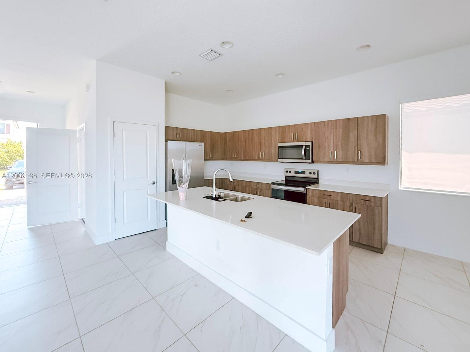 A modern kitchen features a white island, light wood cabinets, and white tile flooring — 5639 Argento Drive # 5639, Ave Maria FL 34142, AVE MARIA, FL