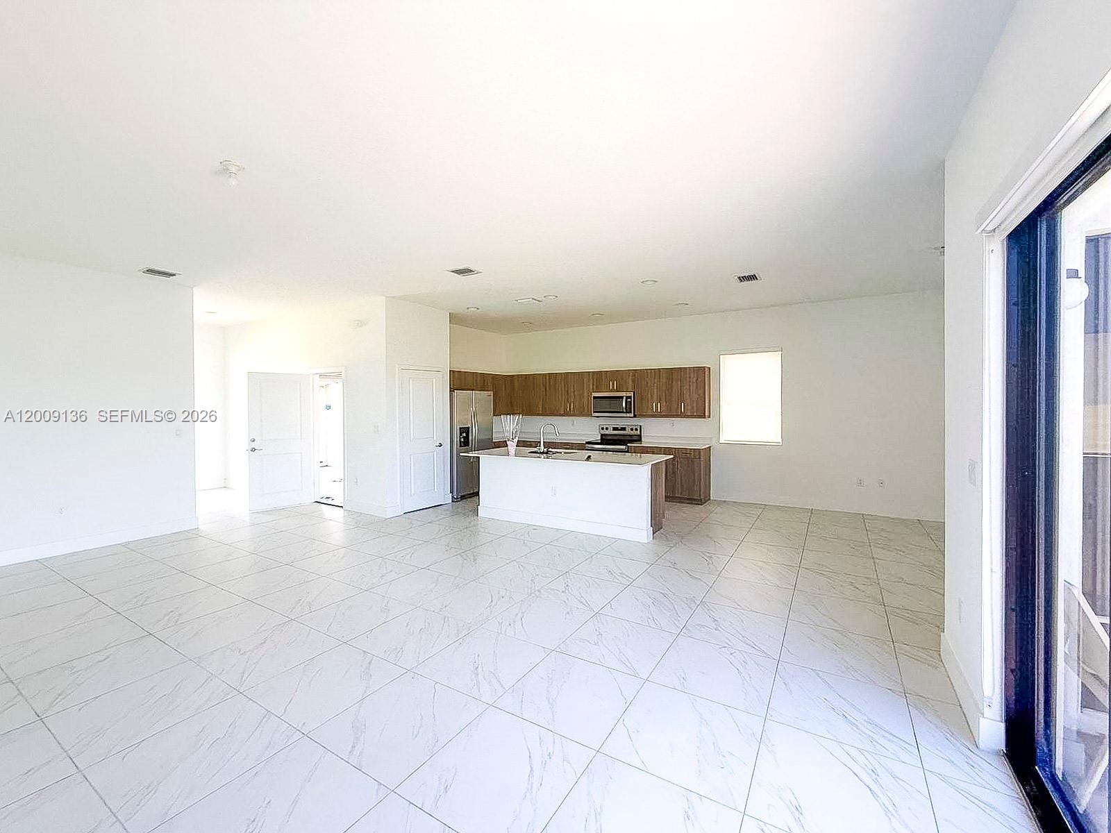 An open-concept kitchen features a white island, wood-toned cabinetry, and light-colored marble-patterned tile flooring — 5639 Argento Drive # 5639, Ave Maria FL 34142, AVE MARIA, FL