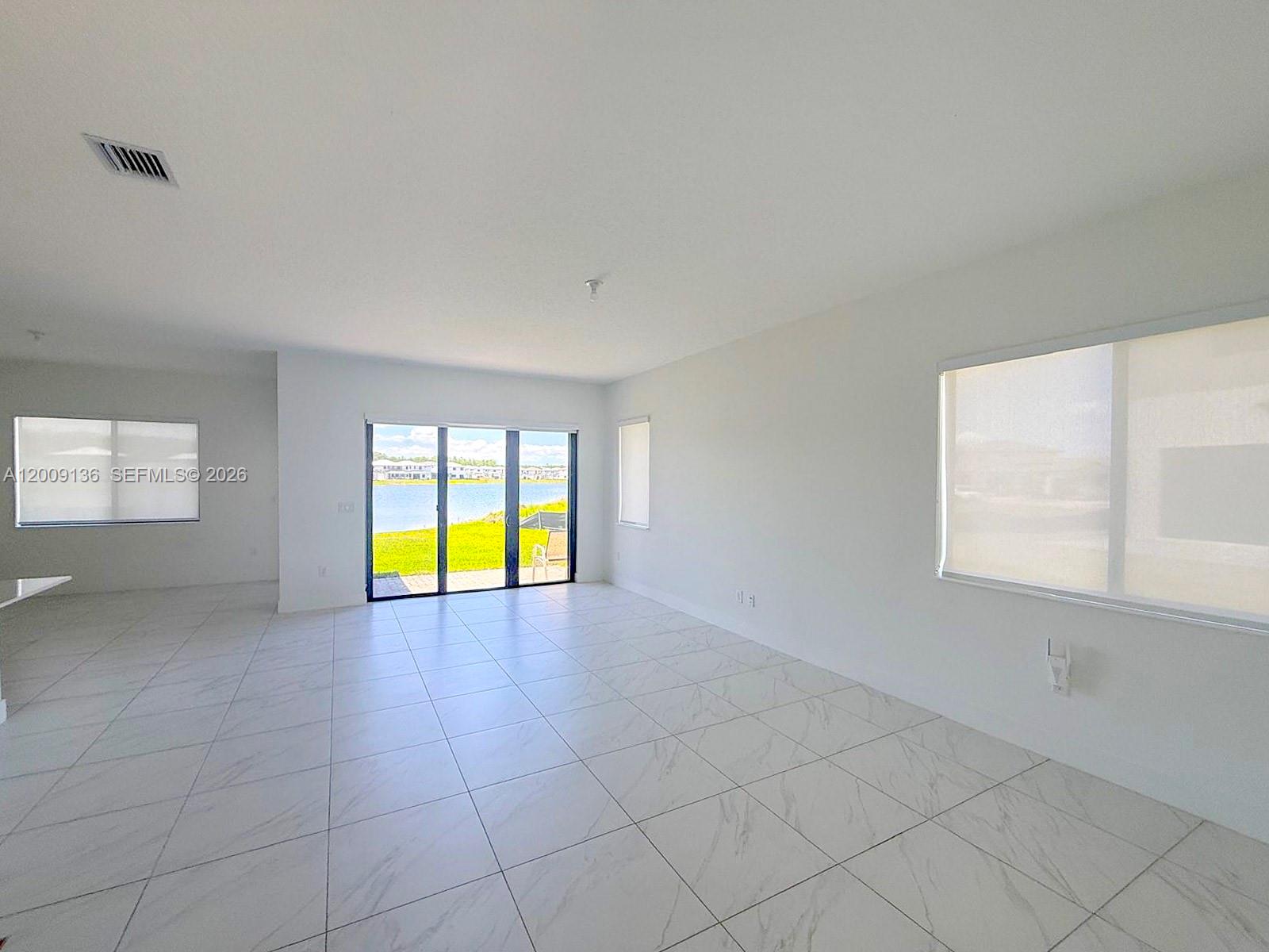 A bright, empty living room features white tile flooring, large windows, and sliding glass doors — 5639 Argento Drive # 5639, Ave Maria FL 34142, AVE MARIA, FL