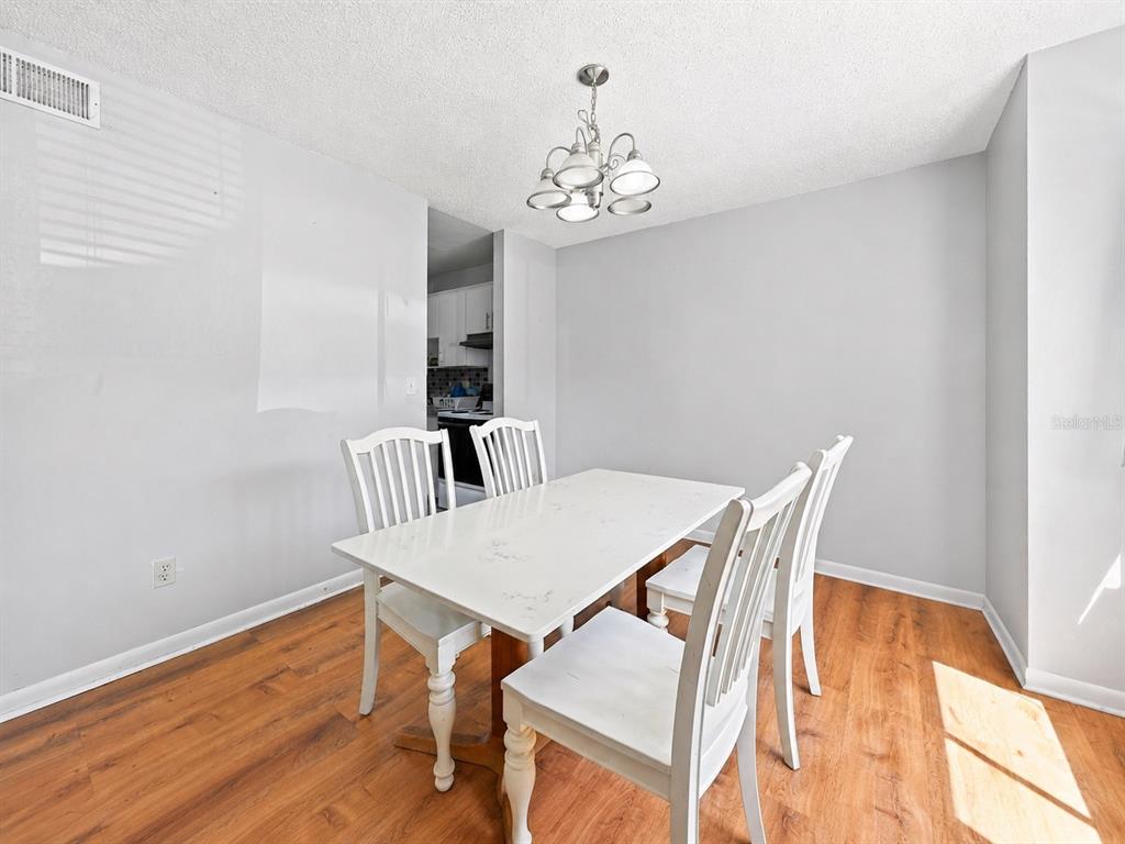 A dining area with a white table, four chairs, a chandelier, and wood-look flooring — 5137 PICADILLY CIRCUS COURT UNIT 3, ORLANDO, FL