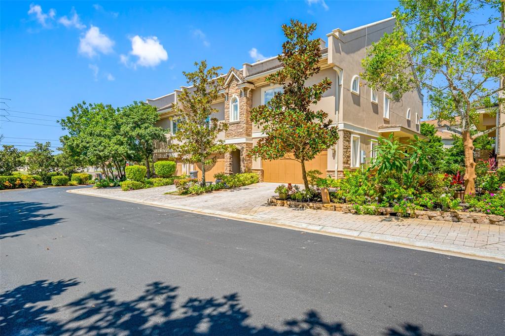 A multi-story townhouse with a stone facade, tan stucco walls, and attached garages — 1425 HILLSIDE LANDING DRIVE, TARPON SPRINGS, FL