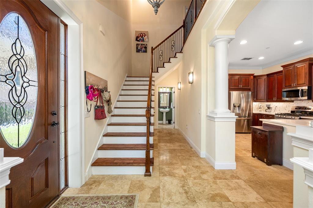 An entryway features a wooden staircase, tile flooring, and an open view into the kitchen — 1425 HILLSIDE LANDING DRIVE, TARPON SPRINGS, FL