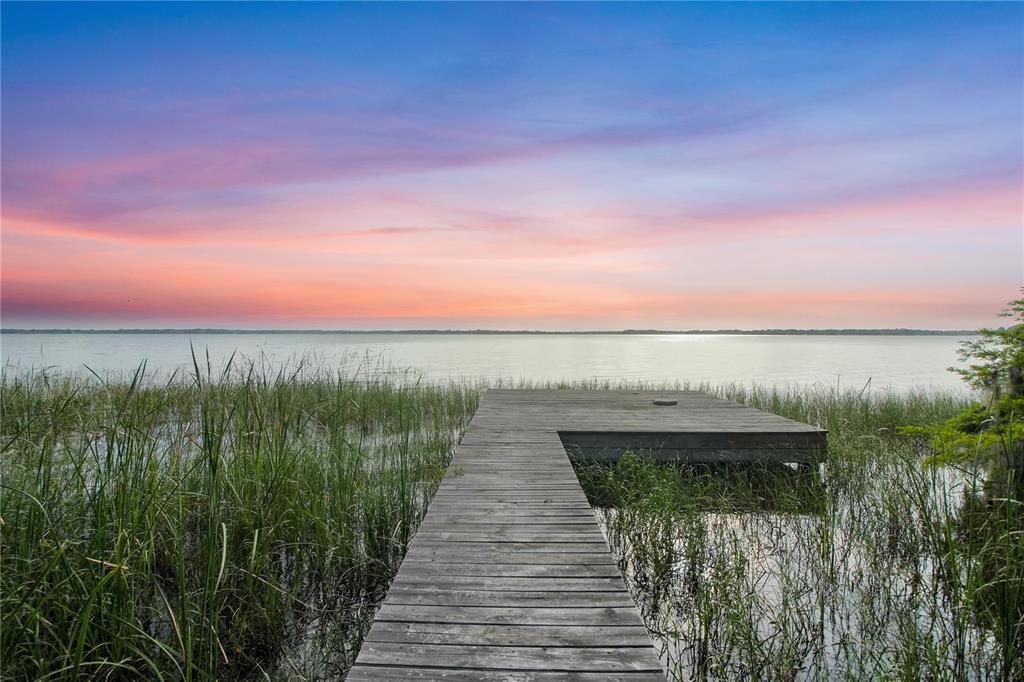 A wooden dock extends into a lake surrounded by tall grass under a sunset sky — 30437 ORANGE DRIVE, LEESBURG, FL