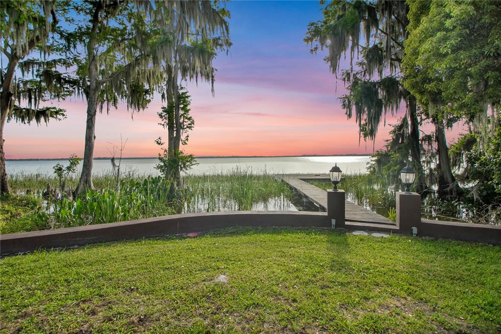 A grassy backyard leads to a wooden dock extending into a lake at sunset — 30437 ORANGE DRIVE, LEESBURG, FL