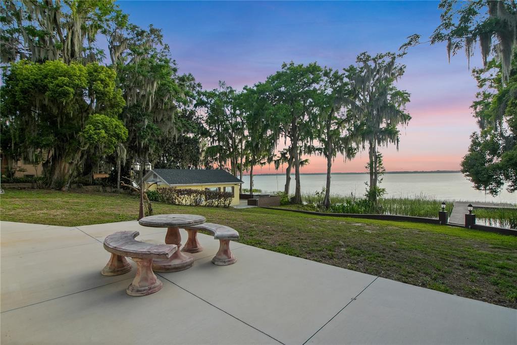 A concrete patio with a stone table and benches overlooks a lake at sunset — 30437 ORANGE DRIVE, LEESBURG, FL