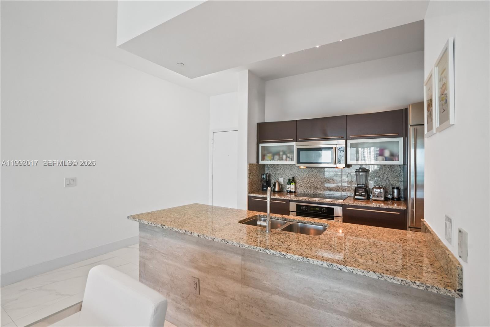 A modern kitchen features dark brown cabinets, granite countertops, and a central island with sink — 950 Brickell Bay Dr # 4101, Miami FL 33131, MIAMI, FL