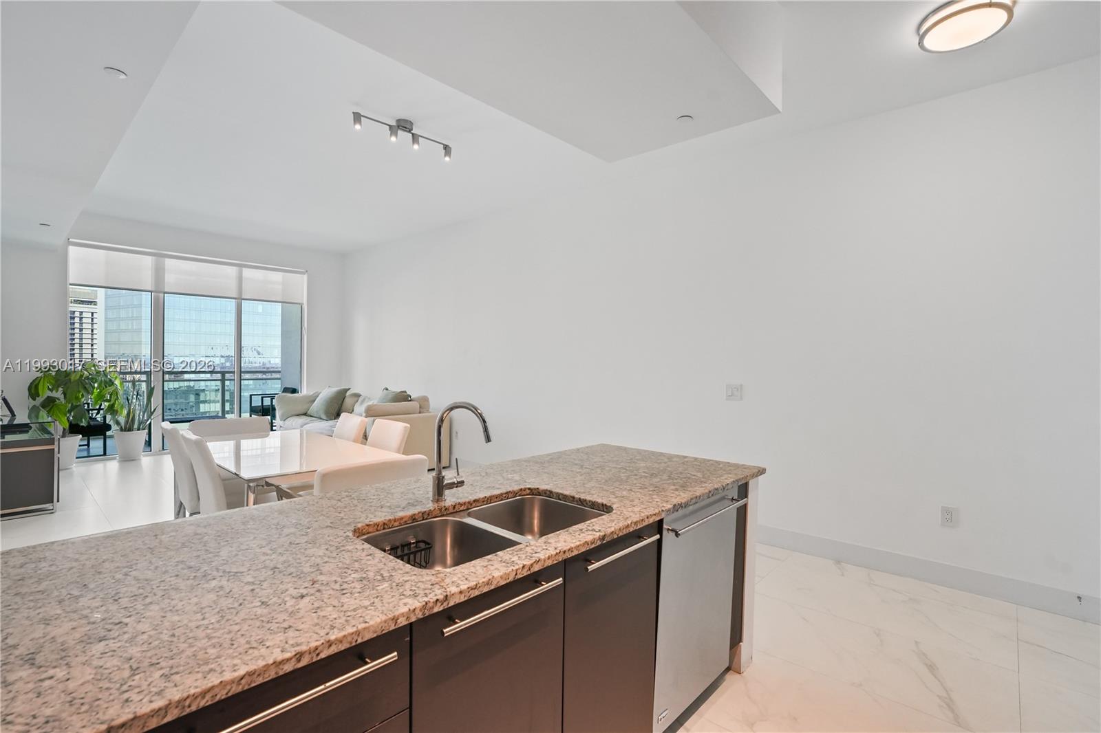 A kitchen island with granite countertops and dark cabinets overlooks a dining and living area — 950 Brickell Bay Dr # 4101, Miami FL 33131, MIAMI, FL