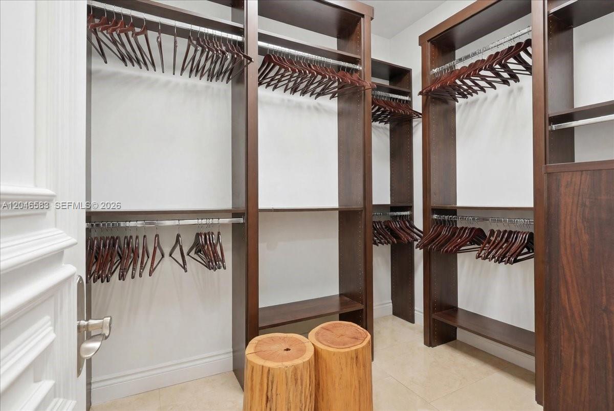 A walk-in closet features dark wood shelving, hanging rods, and two wooden stump stools — 4734 Sunset Drive, Miami FL 33143, MIAMI, FL
