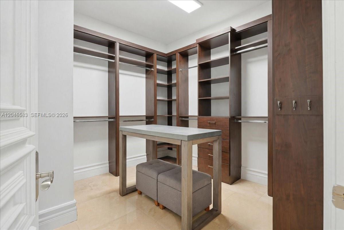A walk-in closet features dark wood shelving, hanging rods, and a central island with seating — 4734 Sunset Drive, Miami FL 33143, MIAMI, FL