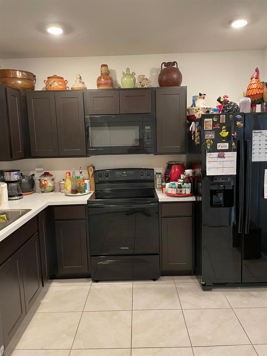 A kitchen features dark brown cabinets, black appliances, and a tiled floor — 556 NE 5th St, Florida City FL 33034, FLORIDA CITY, FL