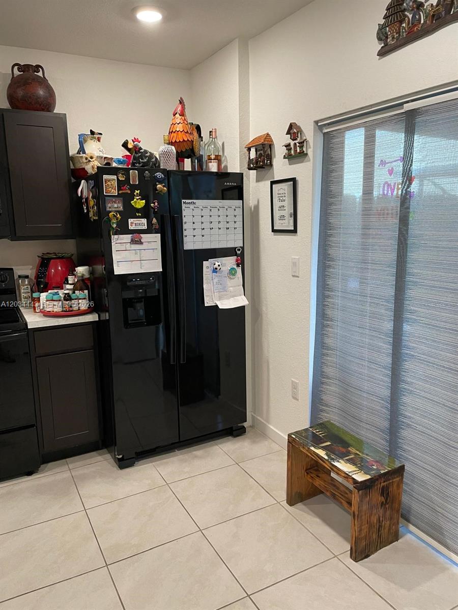 A kitchen features dark cabinets, a black refrigerator with a calendar, and a small wooden bench — 556 NE 5th St, Florida City FL 33034, FLORIDA CITY, FL
