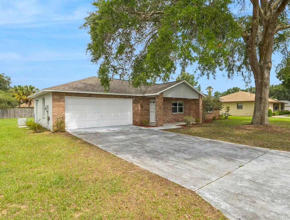 A single-story brick house with a two-car garage and a large tree in the yard — 261 SE 61ST COURT, OCALA, FL