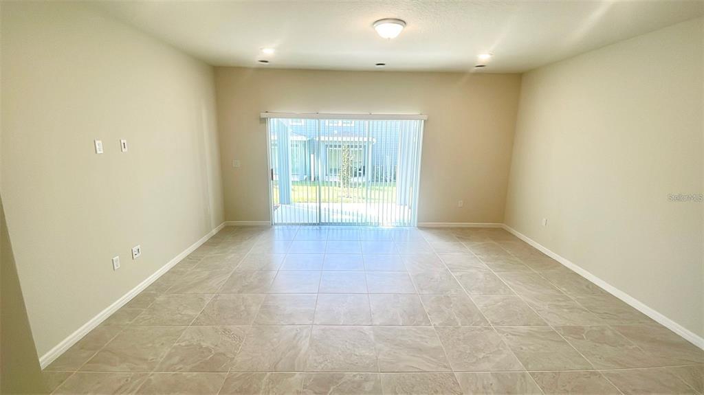 An empty room with beige tile flooring and a sliding glass door leading outside — 2571 WINSOME WAY, DAVENPORT, FL
