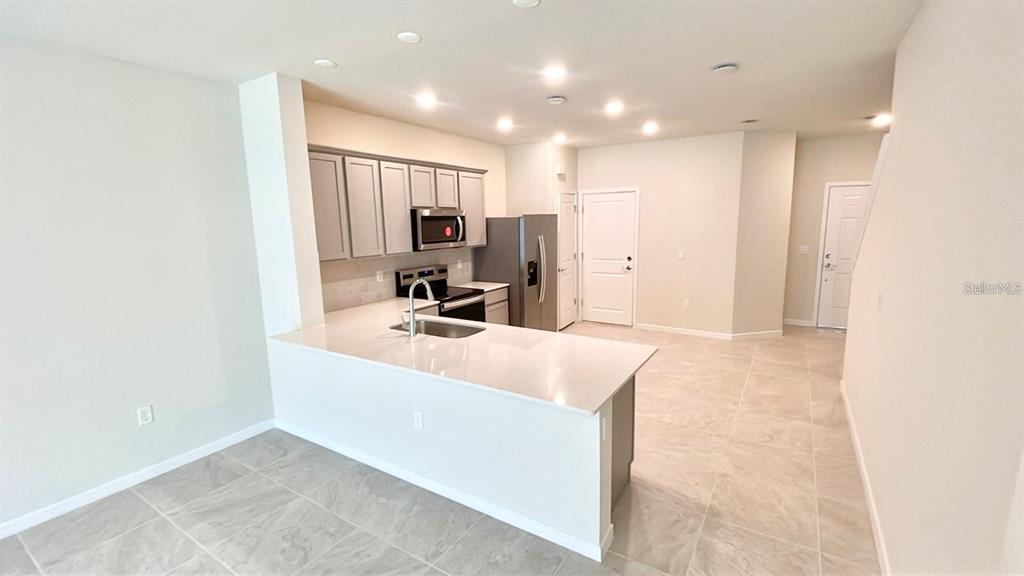 A kitchen features gray cabinets, stainless steel appliances, and a white quartz breakfast bar — 2571 WINSOME WAY, DAVENPORT, FL
