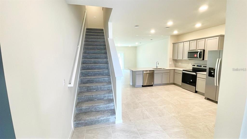 A staircase with gray carpet leads upward next to an open-concept kitchen with light cabinetry — 2571 WINSOME WAY, DAVENPORT, FL