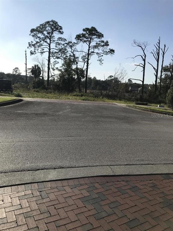 A paved street leads toward a vacant lot with several tall trees under a clear sky — Parcel 1 - 607 OVIEDO BOULEVARD, OVIEDO, FL