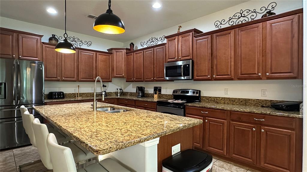 A kitchen features wood cabinets, granite countertops, a large island, and stainless steel appliances — 8860 CANDY PALM ROAD, KISSIMMEE, FL