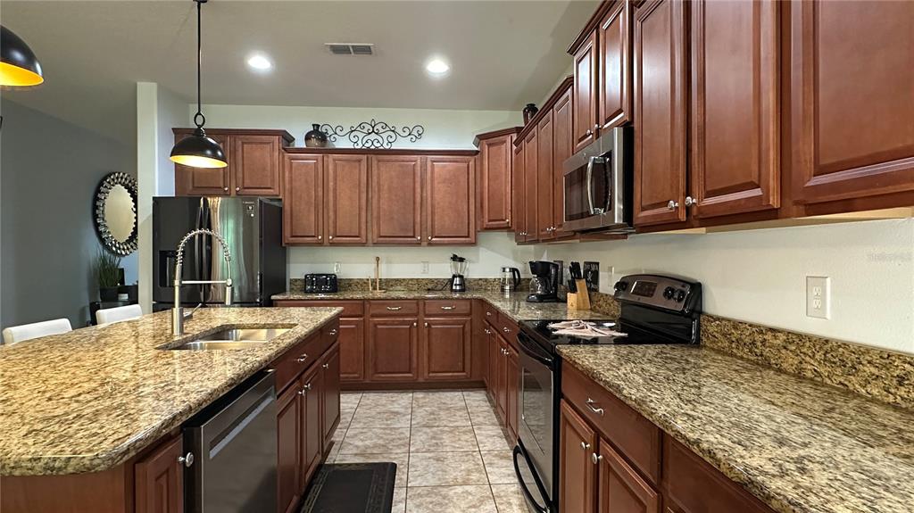 A kitchen features wood cabinets, granite countertops, stainless steel appliances, and a central island — 8860 CANDY PALM ROAD, KISSIMMEE, FL
