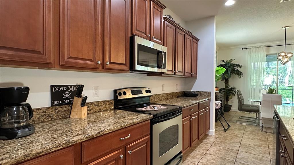 A kitchen features wooden cabinets, granite countertops, stainless steel appliances, and tile flooring — 8860 CANDY PALM ROAD, KISSIMMEE, FL