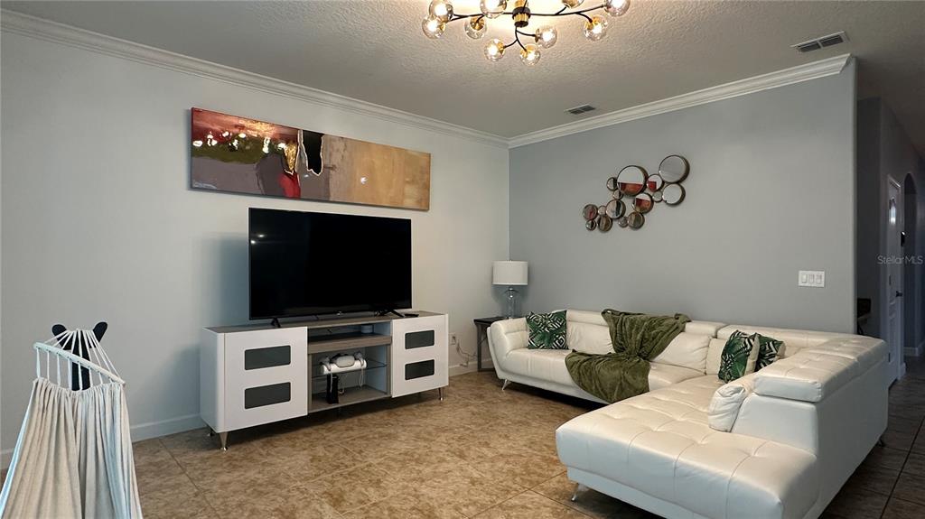 A living room features a white sectional sofa, a television on a console, and a chandelier — 8860 CANDY PALM ROAD, KISSIMMEE, FL