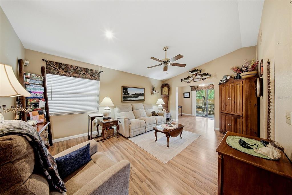 A living room features a vaulted ceiling, wood-look flooring, a ceiling fan, and neutral furniture — 38648 FERM CIRCLE, ZEPHYRHILLS, FL