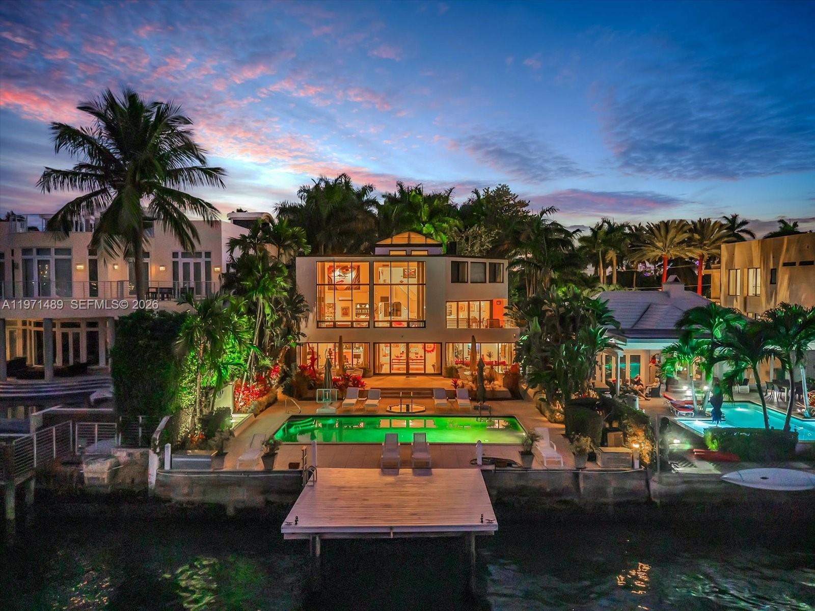 An aerial view of a waterfront house with a pool, dock, and palm trees at sunset — 279 N Hibiscus Dr, Miami Beach FL 33139, MIAMI BEACH, FL