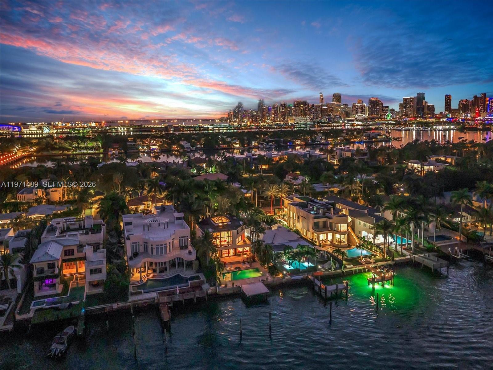 An aerial view of waterfront luxury homes at dusk with a city skyline in the background — 279 N Hibiscus Dr, Miami Beach FL 33139, MIAMI BEACH, FL