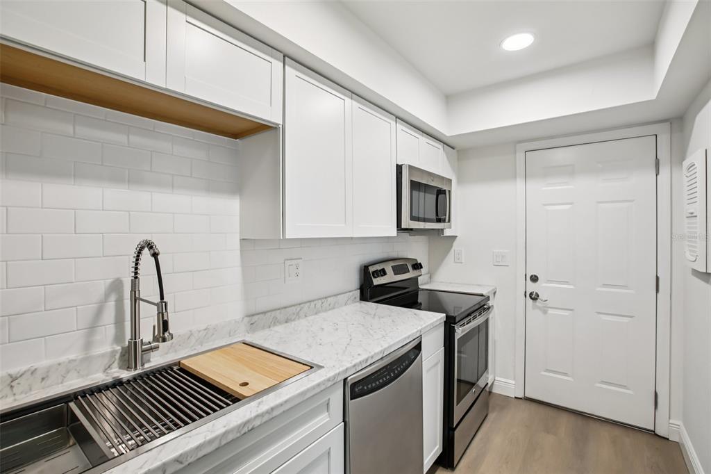 A modern kitchen features white cabinets, marble-look countertops, stainless steel appliances, and a subway tile backsplash — 2906 LICHEN LANE UNIT B, CLEARWATER, FL