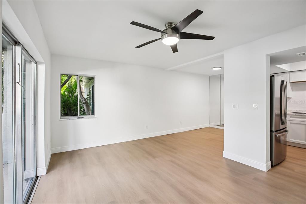 A bright, empty room with light wood-look flooring, a ceiling fan, and a sliding glass door — 2906 LICHEN LANE UNIT B, CLEARWATER, FL